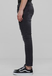 Jeans negros ajustados con un acabado desgastado, que cuentan con bolsillos y una cintura de altura media. Combinados con zapatillas negras con acentos blancos.