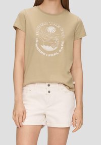 Khaki t-shirt with short sleeves and a round neckline features white graphic text and design. Paired with light-colored denim shorts.
