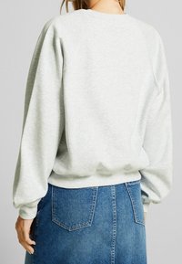 Felpa grigia chiara con scollatura rotonda e maniche raglan, caratterizzata da un orlo e polsini a costine, abbinata a una gonna in denim blu.