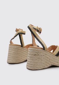Sandalias de cuña con tacón de yute trenzado, detalles en cuero marrón, tiras de lienzo negro y una hebilla en el tobillo. Diseño texturizado y ligero.