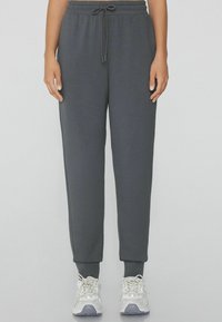 Graue Jogginghose mit einem elastischen Bund und Kordelzug, mit gerippten Knöcheln und weichem Material, kombiniert mit weißen Sportschuhen.