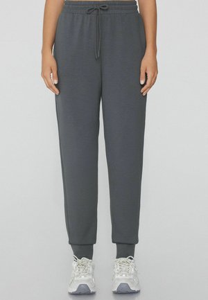 Pantaloni da jogging grigi con vita elastica e lacci, dotati di caviglie elastiche e una texture morbida, abbinati a scarpe sportive bianche.