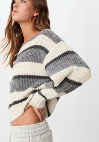 Sweter w paski w odcieniach szarości, kremu i czerni, o luźnym kroju, teksturowanej strukturze i szerokich rękawach. Stylizowany z spodniami z wysokim stanem.