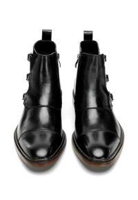 Botas de tobillo de cuero negro con punta afilada, cremalleras laterales y tres hebillas decorativas en los lados exteriores. Textura suave y suela resistente.