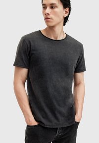 Schwarzes T-Shirt mit kurzen Ärmeln und rundem Ausschnitt, aus weichem Stoff mit einer dezenten gewaschenen Textur, kombiniert mit dunklen Jeans.