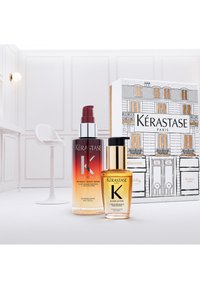 De haarverzorgingsset van Kérastase Paris bevat een bordeauxrood vervaagde fles met het label "Nutritive" en een gouden fles met het label "Elixir Ultime", beide in een ontwerpdoos.