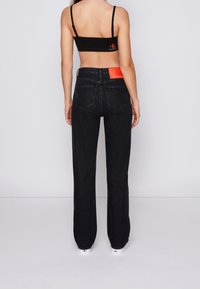 Svarta denimjeans med en avslappnad passform, hög midja och synlig sömnad. En orange Calvin Klein-logotyp är placerad på bakre midjebandet.