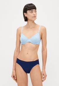 Svetlo modri usnjeni modrček s nastavljivimi naramnicami, v kombinaciji s temno modrimi enobarvnimi bikini hlačkami. Tkanina se zdi gladka z rahlim sijajem.