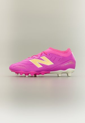 Φωτεινό ροζ ποδοσφαιρικό παπούτσι με κίτρινο λογότυπο "N", ροζ κορδόνια και λευκές τάπες, σχεδιασμένο για παιχνίδι σε σκληρό έδαφος.