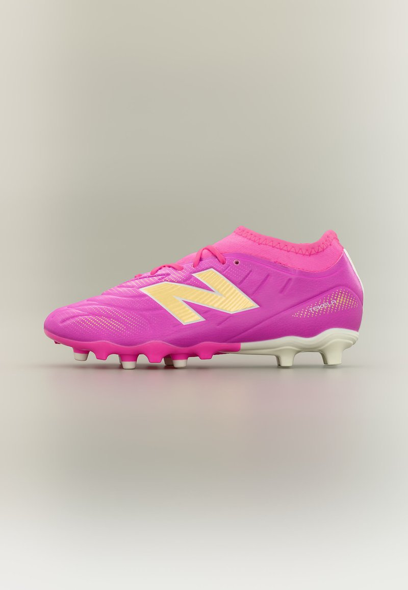 Chaussure de football rose vif avec logo "N" jaune, lacets roses, et crampons blancs, conçue pour jouer sur terrain ferme.