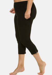 Leggings neri in tessuto elasticizzato, con lunghezza a metà polpaccio, fessure laterali all'orlo e vita elastica. Texture liscia.