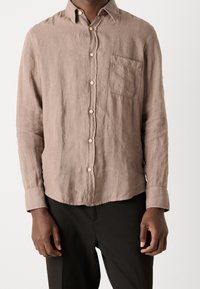 Jasnobrązowa lniana koszula z kołnierzykiem na guziki, kieszenią z przodu i długimi rękawami. Fakturowany materiał z małymi guzikami z przodu.
