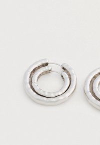 Hõbedatooni vasest topeltringidega ehtepaar valge tausta peal.