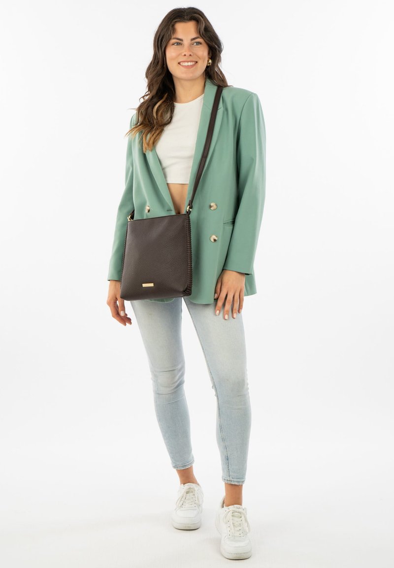 Brown leather crossbody bag with textured surface, contrasting gold hardware, and a rectangular shape. Worn with a green blazer and jeans.