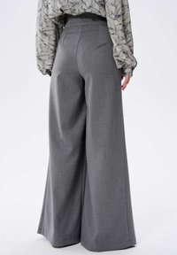 Grijze, wijde broek van gestructureerde stof met een hoge taille. Voorzien van zijzakken en nette naden, weergegeven vanuit de achterkant.