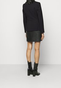 Marinblå kavaj med skräddarsydd passform, långa ärmar och mjuk textur, i kombination med en svart läder minikjol och chunky kängor med klack.