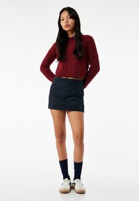 Burgundowy sweter w warkocze, krótki fason. Granatowa mini spódnica, gładka textura. Granatowe skarpetki do kolan, białe trampki z beżowymi akcentami.