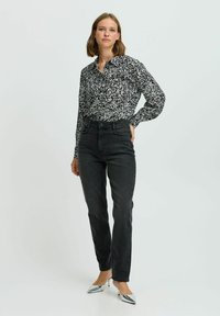 Camicia a maniche lunghe bianca e nera con colletto, abbinata a jeans neri a vita alta e tacchi argentati lucidi.