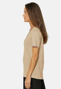 Beige T-shirt met korte mouwen, V-hals en een gemêleerde afwerking langs de kraag en mouwen. Zachte stof en een relaxte pasvorm.