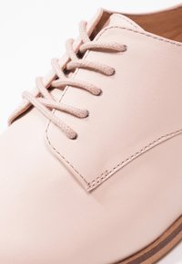 Chaussure habillée en cuir beige avec une finition lisse, dotée de lacets assortis, de détails de couture subtils et d'un design à bout arrondi.