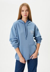 Sudadera con capucha de color azul claro, hecha de una tela suave. Presenta un bolsillo frontal y texto impreso en el pecho. Diseño holgado con mangas acampanadas.