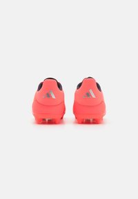 Botas de fútbol rosa brillante con un acabado texturizado, con acentos negros y tres rayas plateadas en la parte posterior. Clavos moldeados para tracción.