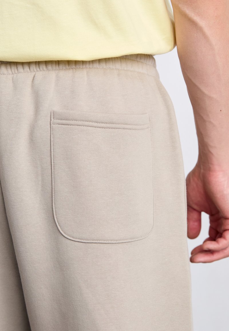 Beige Jogginghose mit einer Gesäßtasche, aus weichem Stoff gefertigt, mit einem elastischen Bund und glatter Textur.