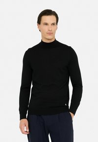 Maglione a collo alto nero in materiale morbido, design aderente con maniche lunghe. Presenta un'etichetta logo discreta all'orlo. Abbinato a pantaloni blu scuro.