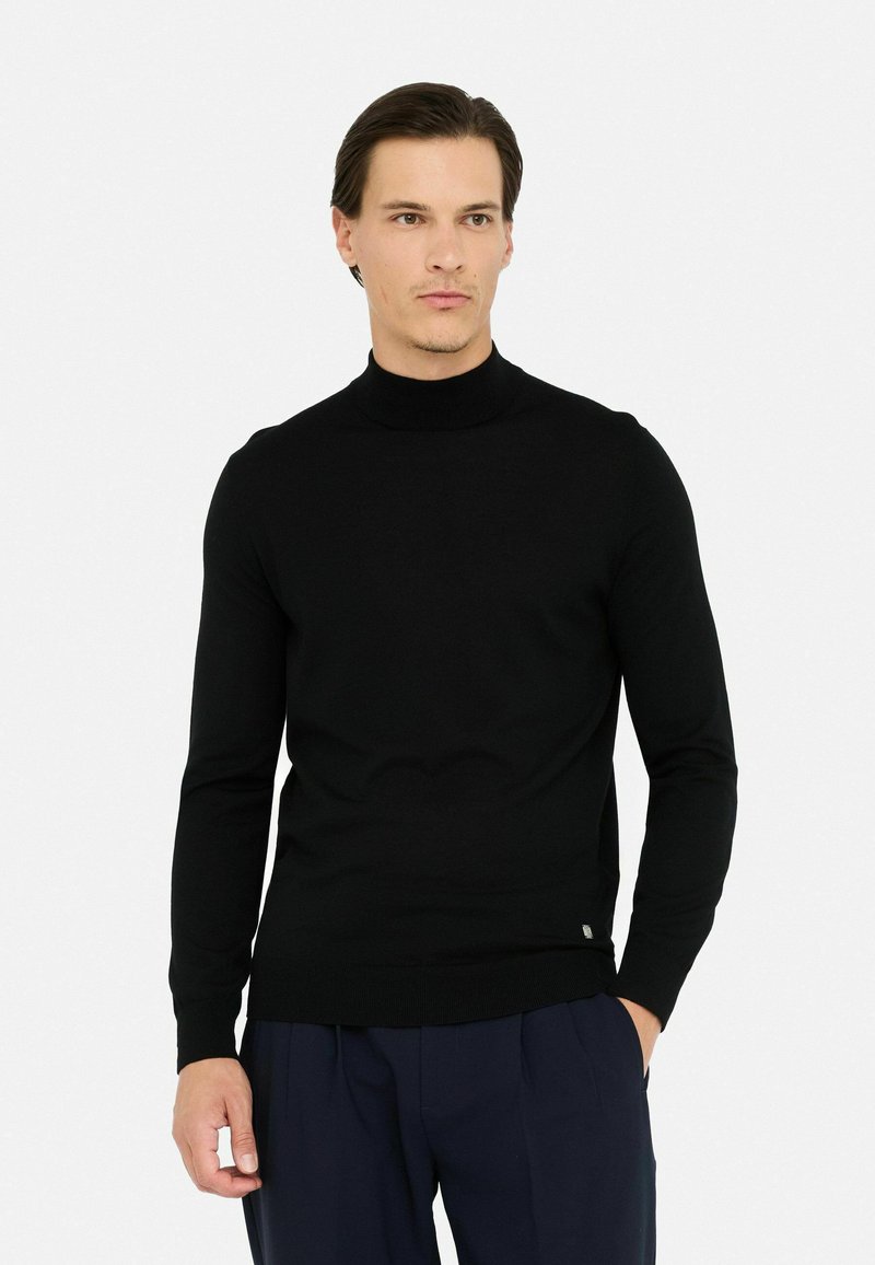 Maglione a collo alto nero in materiale morbido, design aderente con maniche lunghe. Presenta un'etichetta logo discreta all'orlo. Abbinato a pantaloni blu scuro.