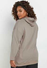 Vaalea ruskea huppari, jossa on pitkät hihat, löysä istuvuus ja ribbitekniikalla tehty helma. Pehmeä kangas, jossa ei ole näkyviä kuvioita tai metalliosia.