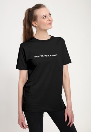Sort bomuld t-shirt med hvid tekst, der lyder "GLÆDELIG SANKT PATRICKS DAG!" Rund hals, korte ærmer, afslappet pasform.