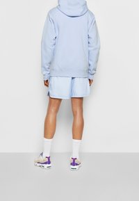 Ljusblå huvtröja med framficka, kombinerad med matchande ljusblå shorts. Skorna har flerfärgade accenter och vita strumpor.