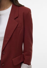 Czerwony bawełniany żakiet z pojedynczym guzikiem, klapami typu notch i kieszonką naszywaną; noszony na białej koszuli z paskowanym mankietem.