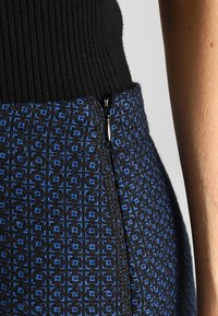 Falda de estampado negro y azul con cintura acanalada, que presenta un cierre de cremallera discreto en el lateral. Tejido texturizado con diseño geométrico.