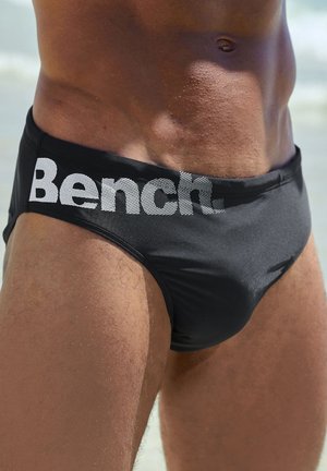 Schwarze Schwimmslips mit einem strukturierten elastischen Bund, auf dem das Logo "Bench." in Weiß gedruckt ist. Glattes Material mit einem eng anliegenden Design.