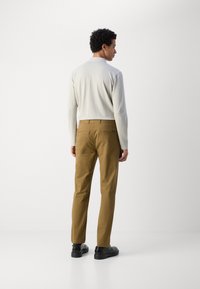 Lys grå langærmet top parret med beige chinos. Outfittet har en slim fit, glat tekstur og sorte sko. Set fra ryggen.