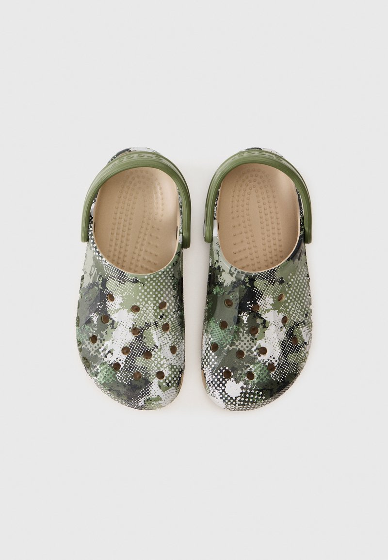 Zoccoli in camo con un motivo a pois verdi e bianchi, realizzati in materiale leggero. Presentano una suola testurizzata e fori di ventilazione.