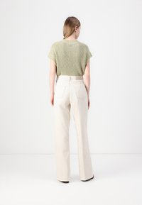 Top de punto verde claro de manga corta combinado con pantalones de tiro alto y pierna ancha en tono beige claro, que destacan por su ajuste relajado y bolsillos traseros.