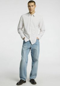 Balta marškiniai su subtilia tekstūra, derinami su šviesiai mėlynomis laisvomis džinsomis ir juodais klasikiais nėriniais. Kasdienis drabužių derinys su paprasta dizainu.