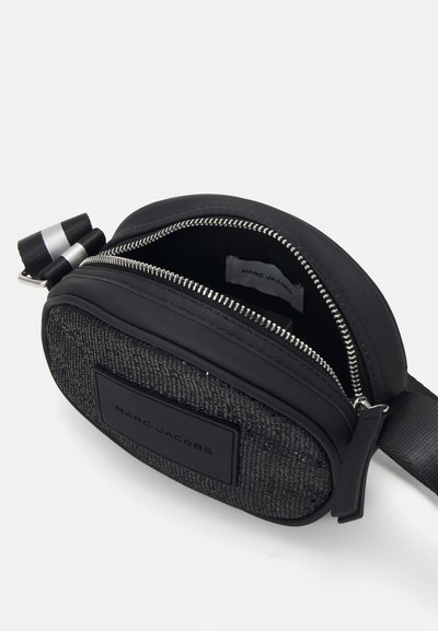Zwarte, gestructureerde schoudertas van materiaal met een zilveren rits en zwarte band. De voorkant heeft een rechthoekig label met "MARC JACOBS" in reliëf.