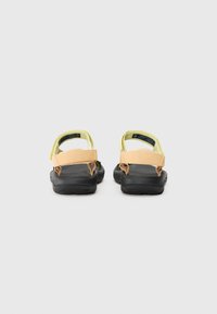 Twee sandalen met een zwarte rubberen zool, voorzien van gele en perzikkleurige stoffen banden. Het ontwerp heeft verstelbare achter- en voorkanten.