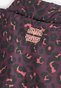 Tessuto viola con macchie di leopardo nere e rosa, con un motivo ornamentale beige ricamato al centro.