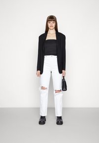 Blazer oversized preto sobre um top preto sem alças, combinado com jeans brancos desgastados e botas de tornozelo pretas e robustas. Pequena bolsa preta.