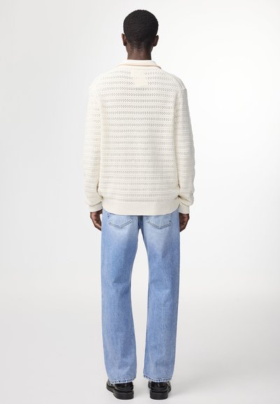 Maglione crema chiaro con un motivo a maglia aperta testurizzato, polsini e orlo a costine, abbinato a jeans dritti azzurri chiari e scarpe nere.