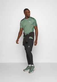 Green athletic t-shirt with patterned sleeves, black leggings with logo, and green sneakers. Black sweatshirt tied at the waist.