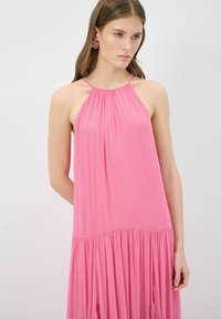 Vestido rosa de tirantes en tejido ligero, con escote fruncido y falda de volantes. Textura suave con un diseño fluido y sin patrones visibles.