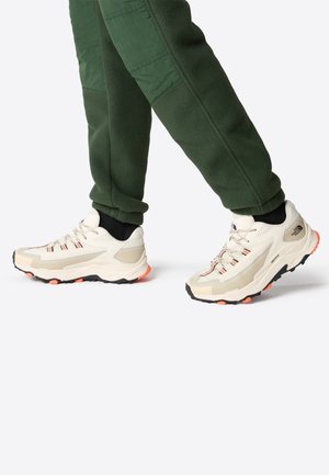 Scarpe sportive beige con pannelli in rete, accentuate da suole nere e arancioni. Il design presenta lacci e una costruzione leggera.