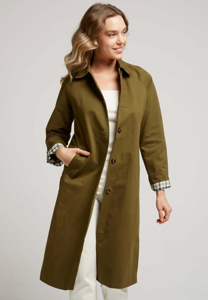 Manteau vert olive à la coupe droite, avec un col, des boutons sur le devant et des accents à carreaux aux poignets. Le matériau semble lisse et durable.