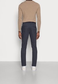 Tmavě modré úzké kalhoty z bavlněné směsi s dvěma zadními kapsami, doplněné béžovou košilí s dlouhým rukávem a bílými teniskami.