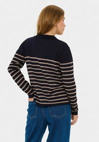 Granatowa koszula z długim rękawem w poziome beżowe paski, z kołnierzykiem i miękką teksturą. Noszona z niebieskimi dżinsami z wysokim stanem.